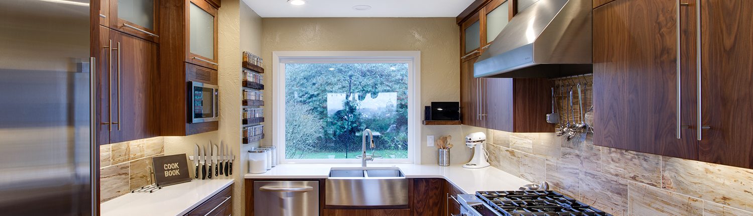 Modern kitchen with wooden cabinets, stainless steel appliances, and a large window overlooking greenery.