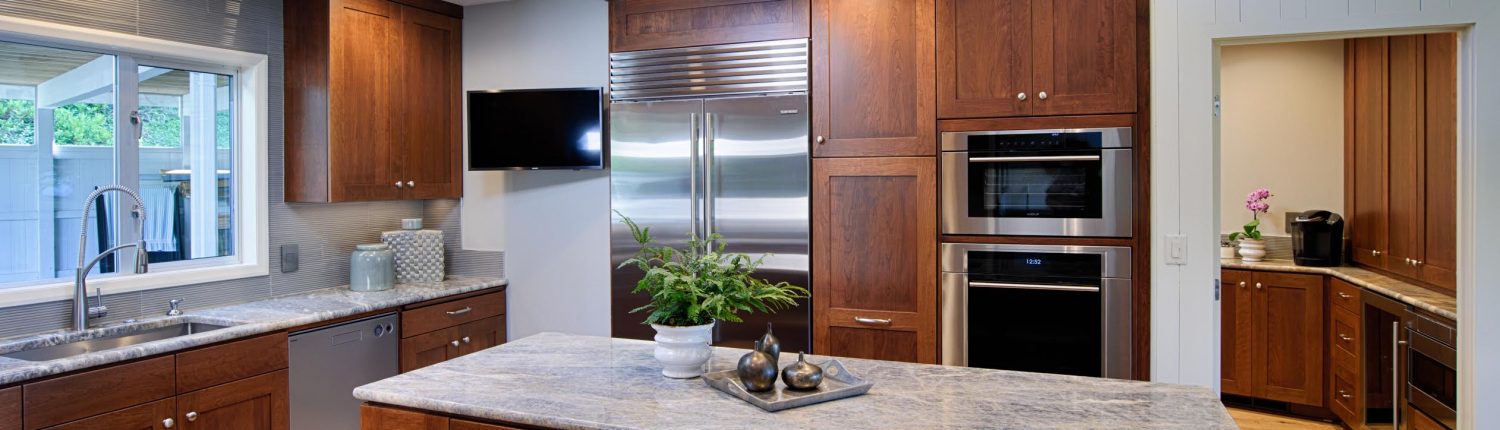 Luxurious kitchen with wooden cabinets, marble countertops, and stainless steel appliances under natural skylight.