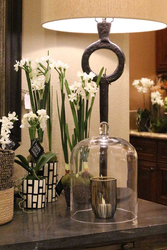 Elegant lamp with white flowers and candle in a glass cloche on a dark table, creating a cozy, inviting ambiance.