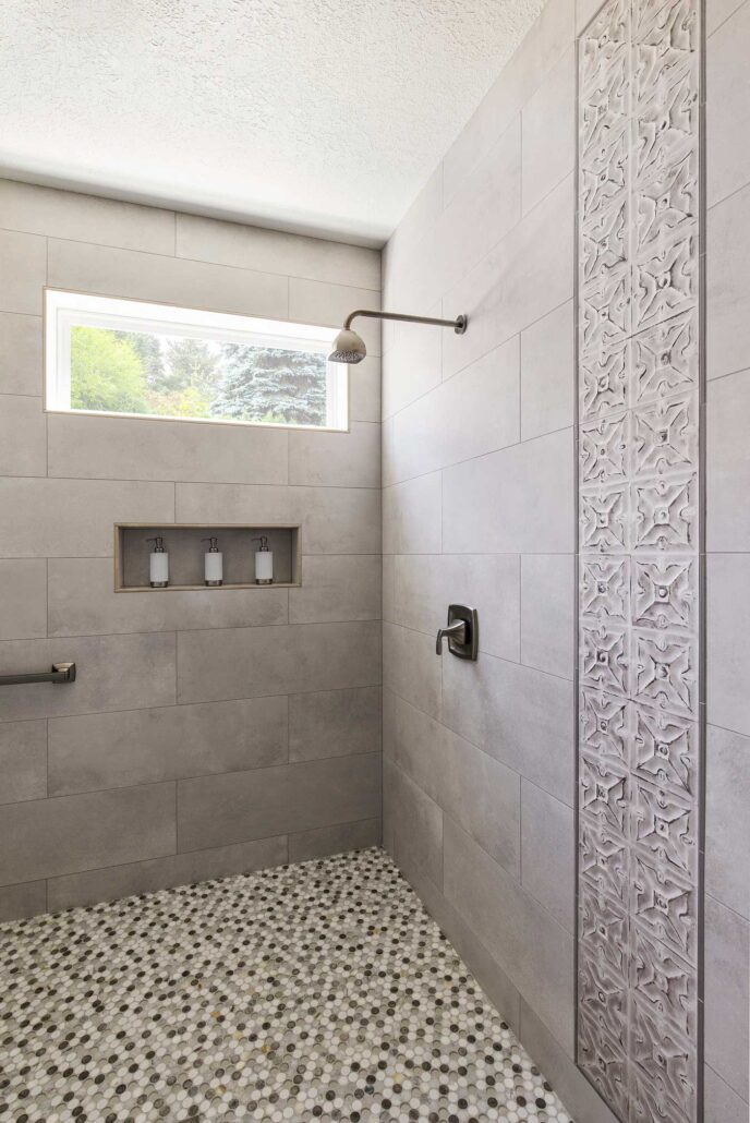 Modern shower with decorative tile accent, pebble floor, and built-in niche under a large horizontal window.