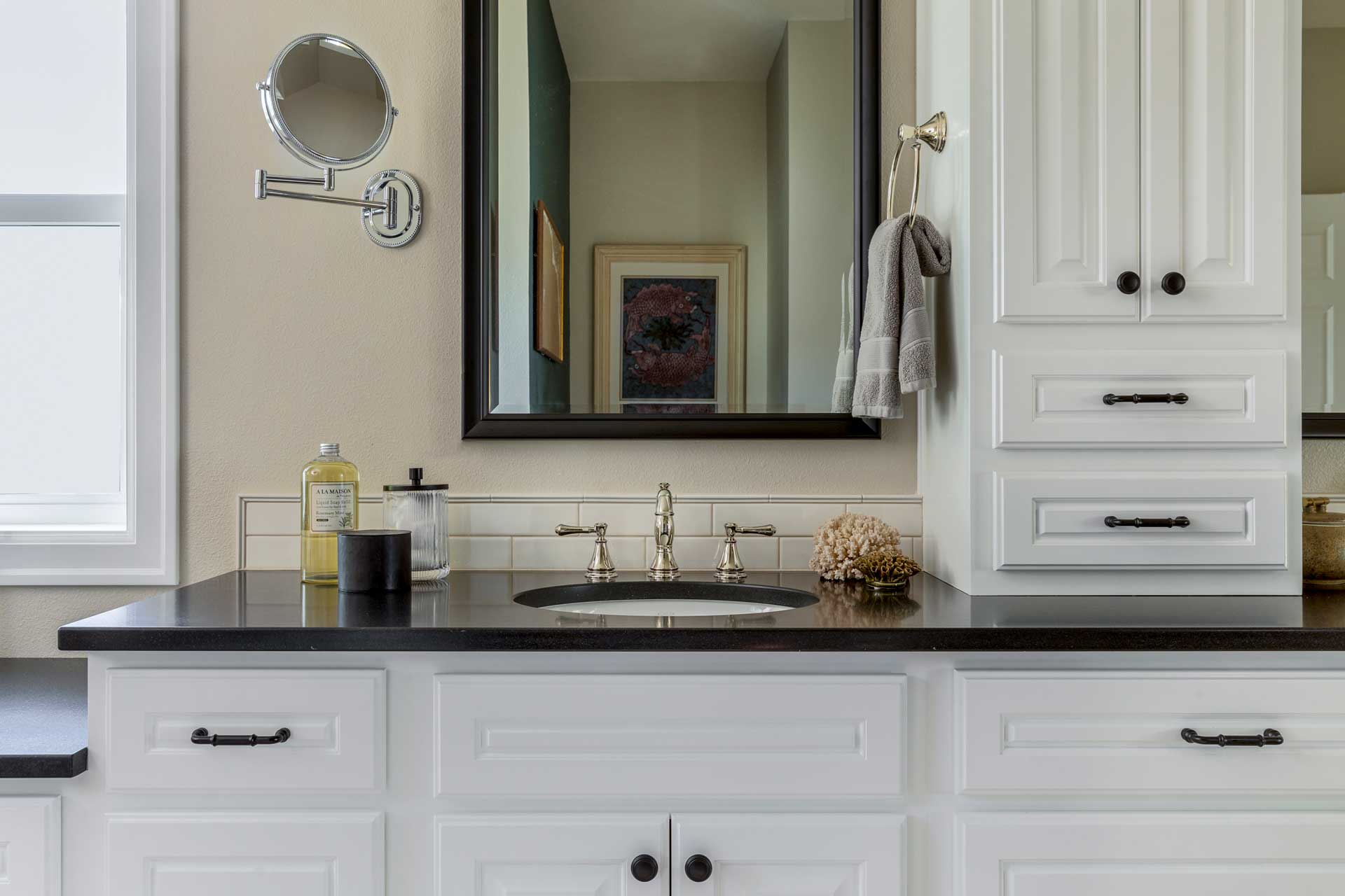 Modern bathroom vanity with black countertop, white cabinets, round mirror, and decorative soap bottle.