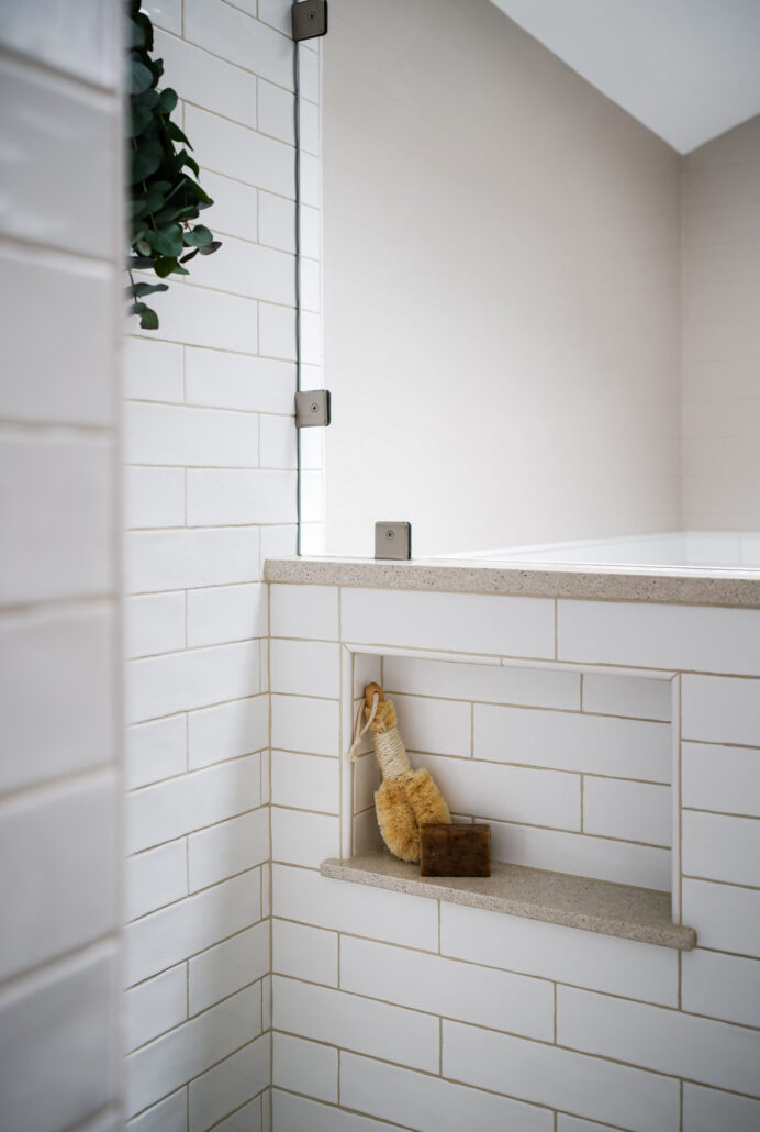 Modern bathroom with white subway tiles, built-in shower shelf holding scrub brush and soap. Clean and minimalistic design.