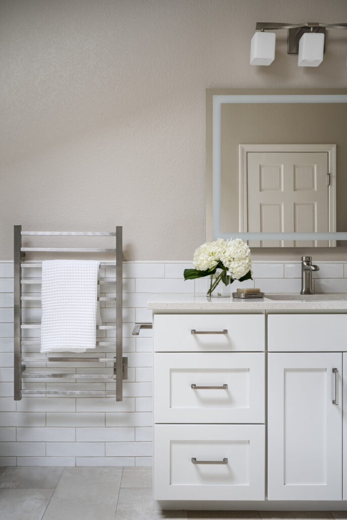 Modern bathroom with white cabinets, metal towel rack, and flowers on the counter for a clean, minimalist look.