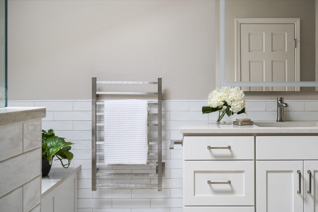 Elegant bathroom interior with a towel rack, white cabinets, and flowers on a countertop.