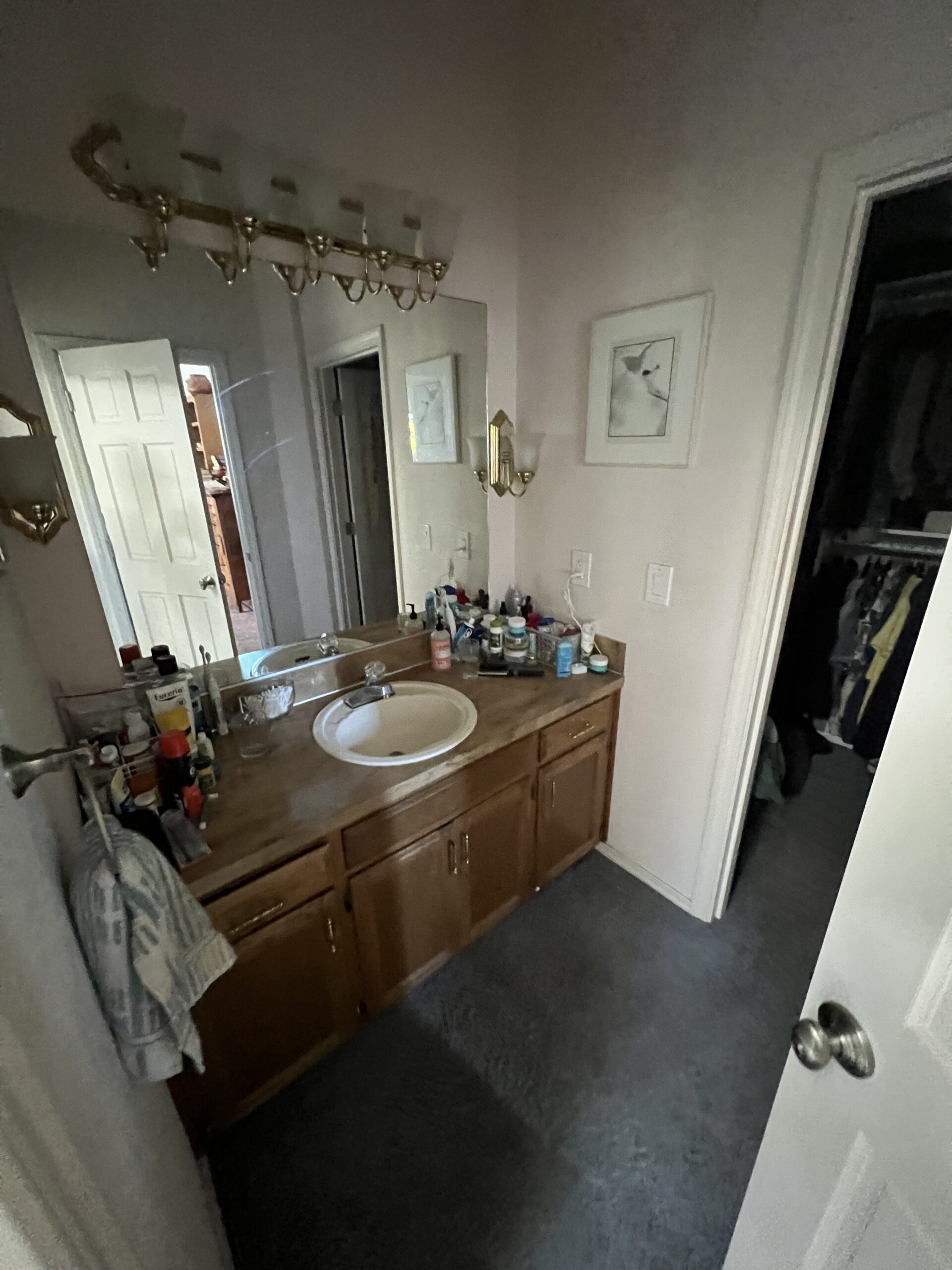 Bathroom vanity with sink, wooden cabinets, and a mirror, surrounded by various toiletries and a towel.