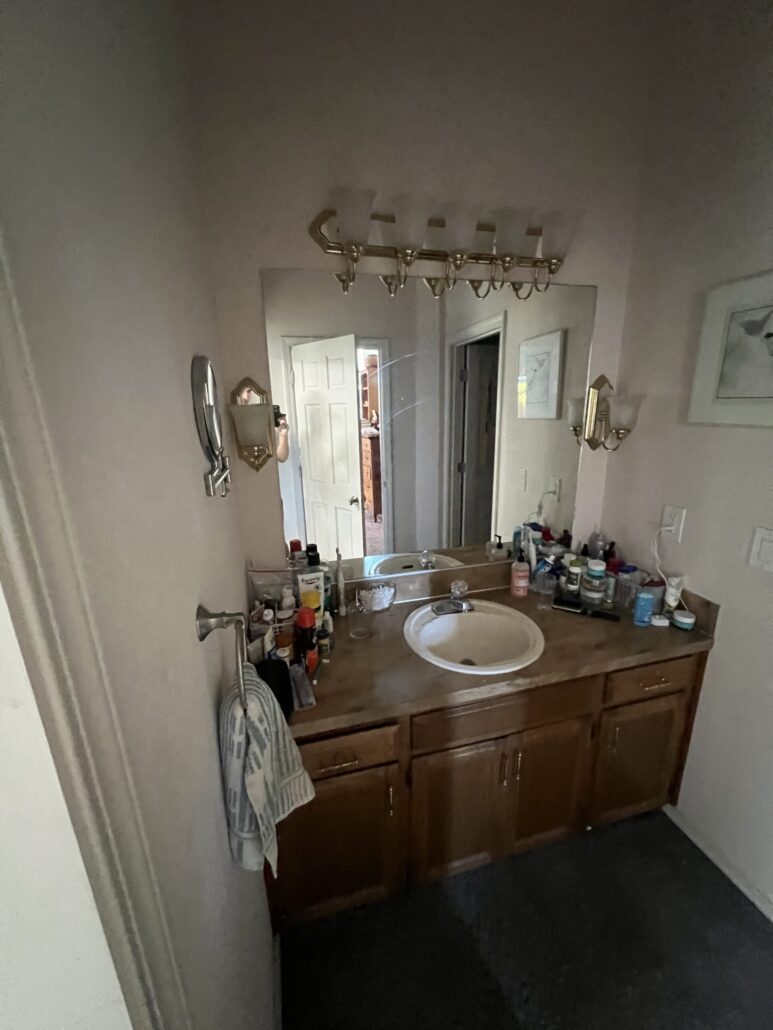 Bathroom vanity with sink, wooden cabinets, and toiletries arranged on the countertop under bright lighting.