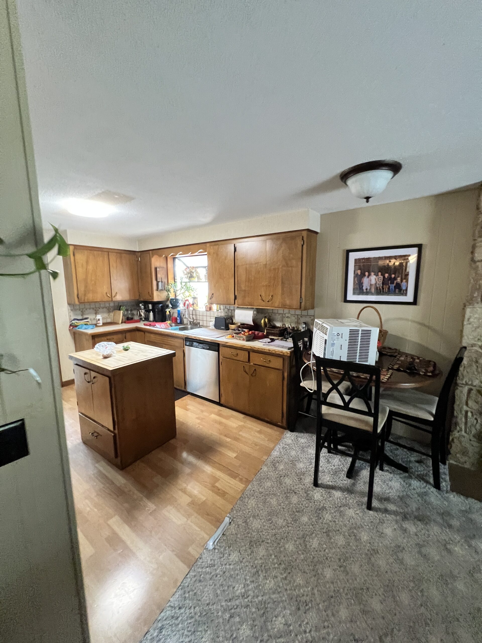Cozy kitchen with wooden cabinets, island, and dining table, featuring a stove, dishwasher, and framed wall art.