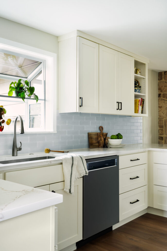 Modern kitchen with white cabinets, grey backsplash, and stainless steel faucet. Bright window with green potted plant.