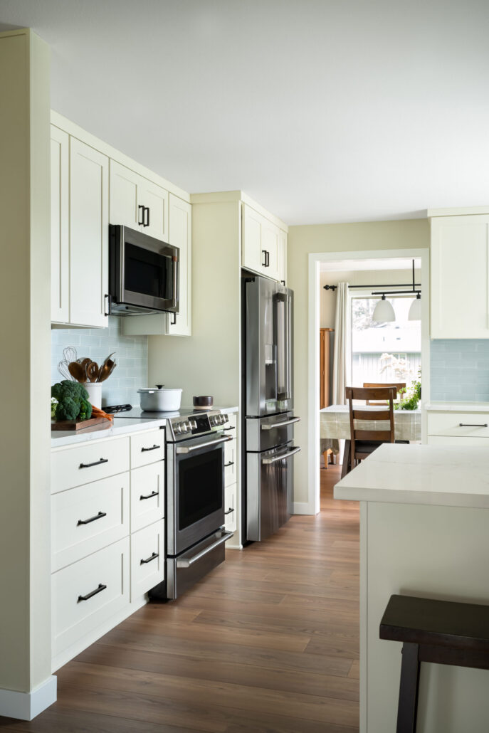 Modern kitchen with cream cabinets, stainless steel appliances, and wood flooring leading to a dining area.