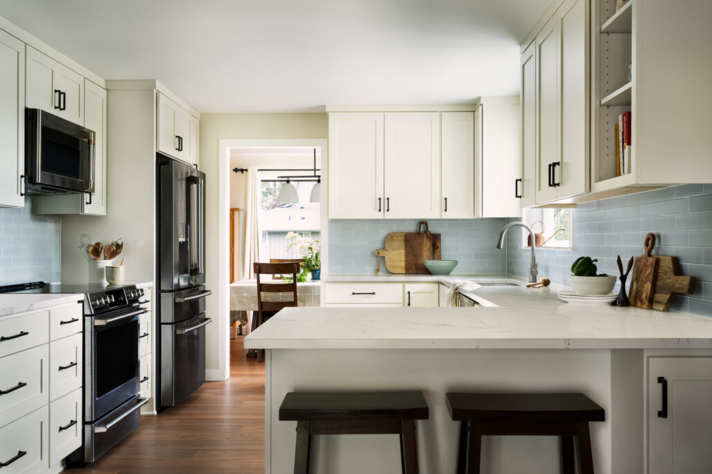 Modern kitchen with white cabinets, black appliances, light blue backsplash, and wooden accents.