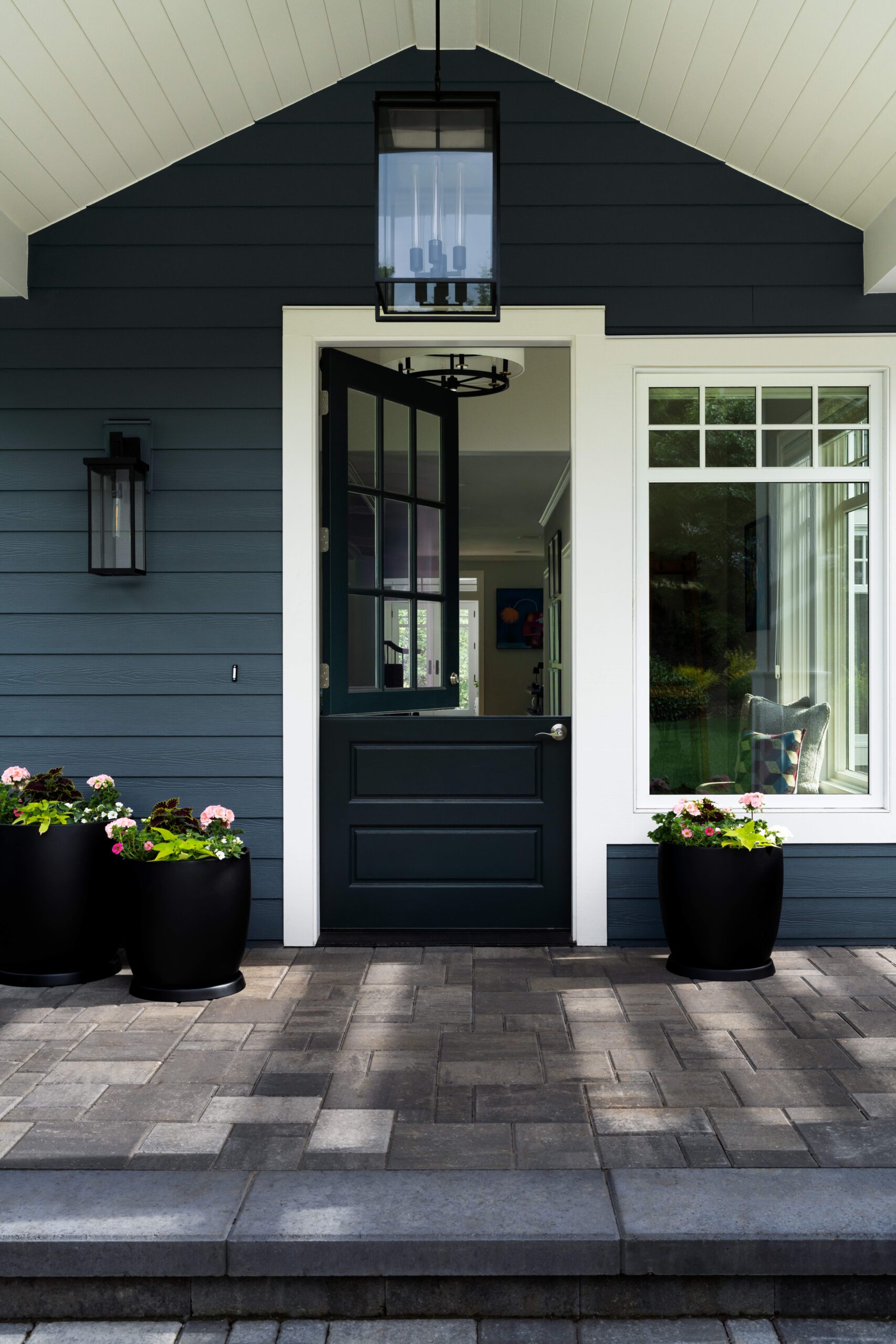 Welcoming front porch with open door, potted flowers, and dark siding under white roof. Modern and inviting entrance.