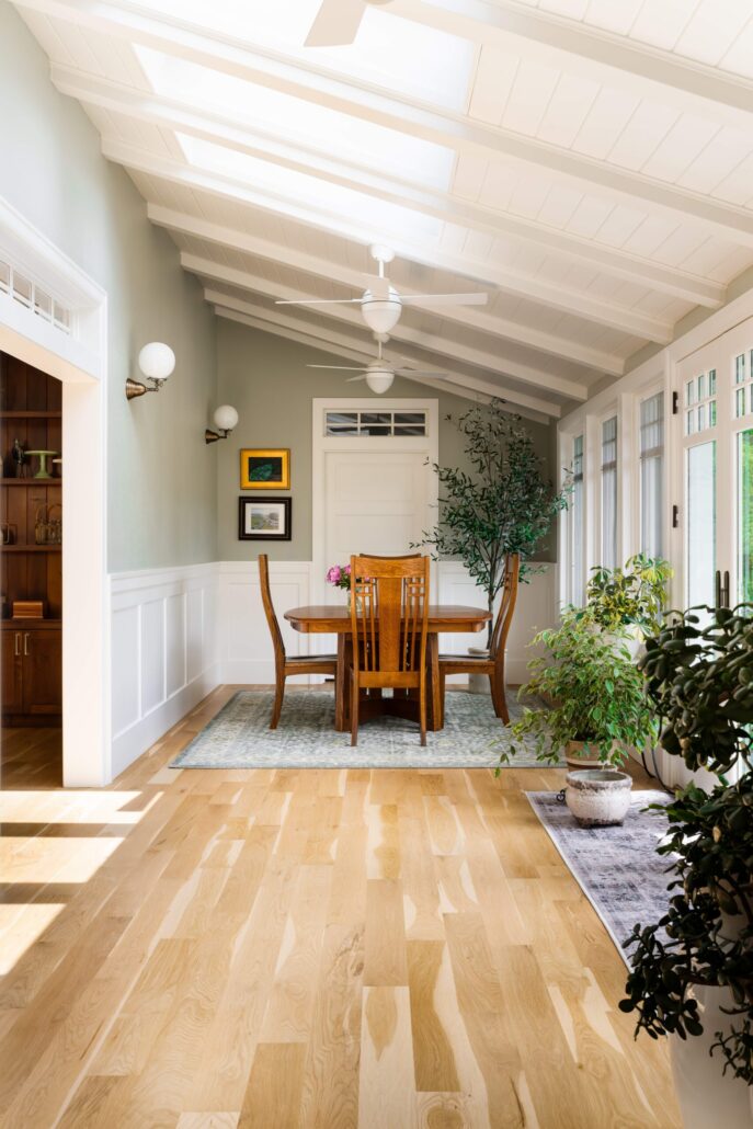 Bright dining room with wooden table, chairs, indoor plants, ceiling fans, and natural light.