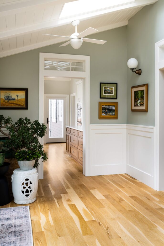 Modern hallway with light wood flooring, decorative plants, and wall art under a ceiling fan.