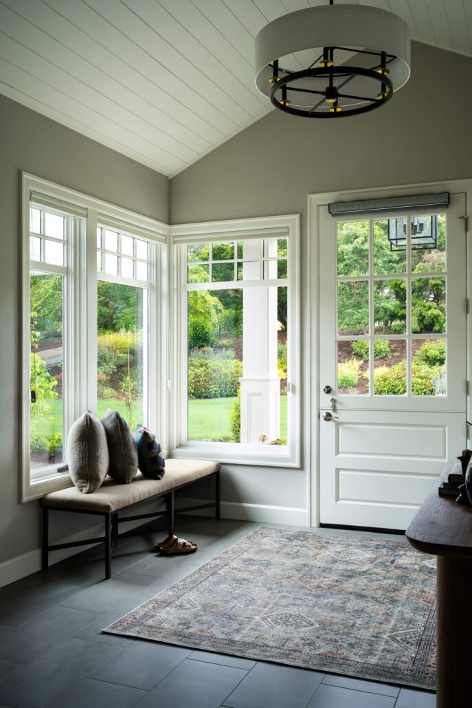 Bright, elegant entryway with large windows, a cozy bench, stylish rug, and garden view.