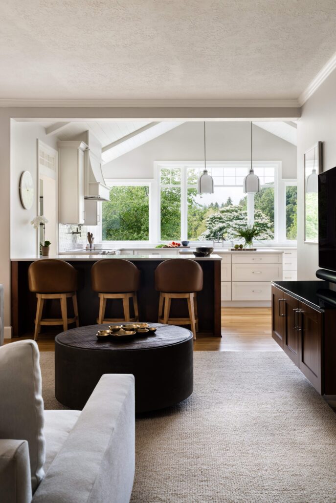 Modern kitchen interior with bar stools, pendant lighting, and large windows overlooking lush greenery.