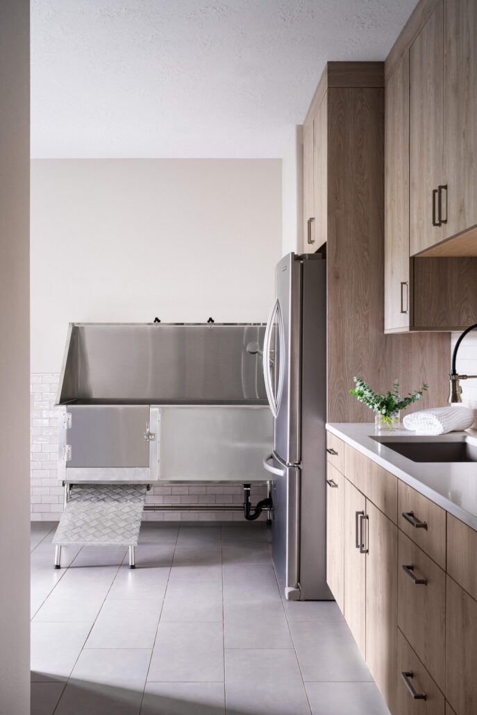 Modern laundry room with wooden cabinets, stainless steel appliances, and a large dog washing station.