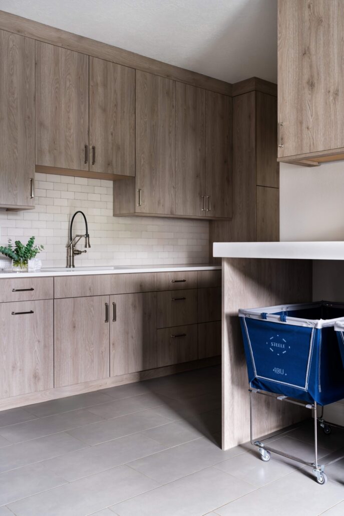 Modern laundry room with wood cabinets, subway tile backsplash, and blue laundry cart on wheels.