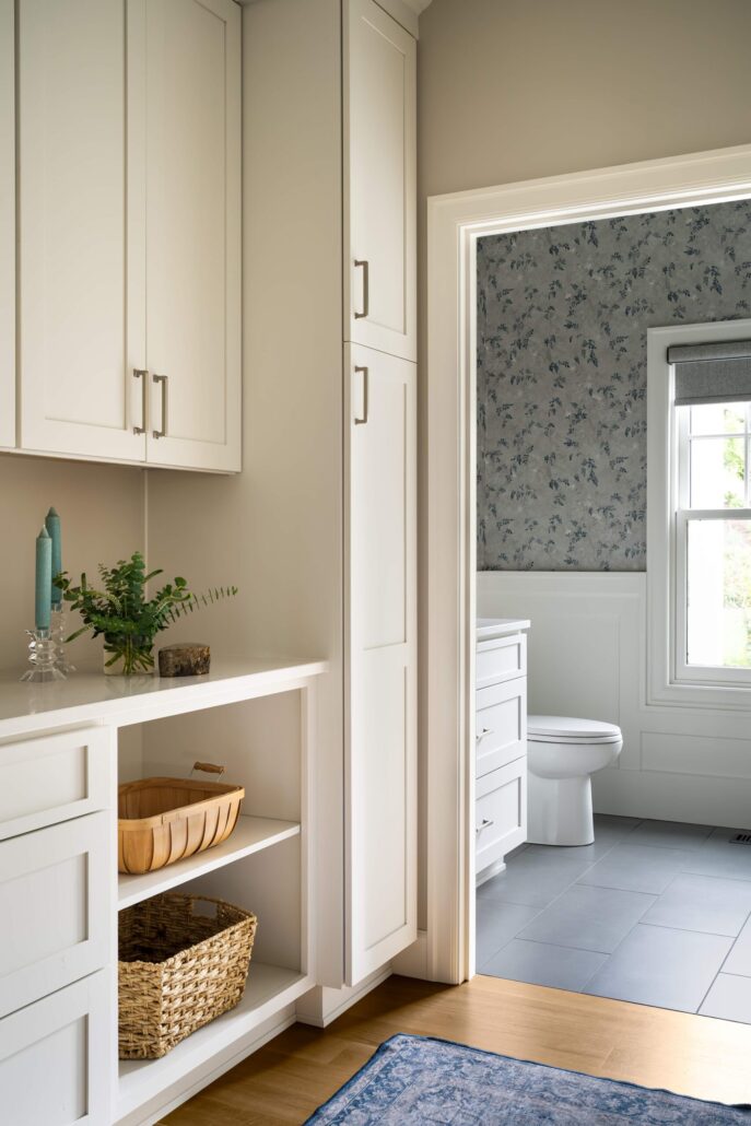 Bright bathroom with floral wallpaper, white cabinets, and cozy decor accents like a wooden basket and green plant.