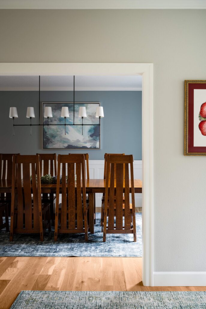 Elegant dining room with wooden chairs, blue rug, modern chandelier, and abstract wall art.