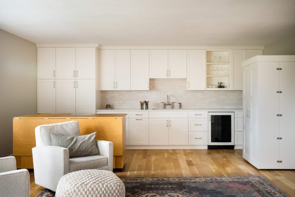 Modern kitchen with white cabinets, wooden island, and cozy seating area on a patterned rug.