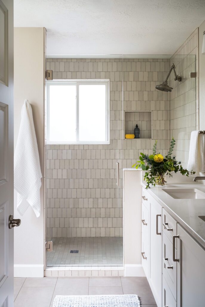 Modern bathroom with tiled walk-in shower, white cabinets, and fresh greenery on the countertop.