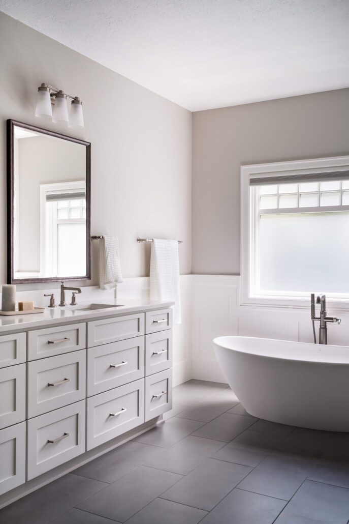 Modern bathroom with sleek vanity, large mirror, freestanding tub, and natural light from window. Elegant interior design.