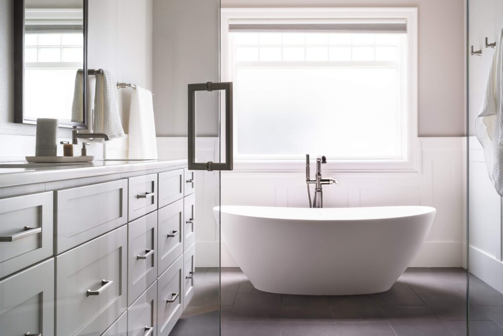 Modern bathroom with freestanding bathtub, large window, sleek cabinetry, and elegant fixtures.