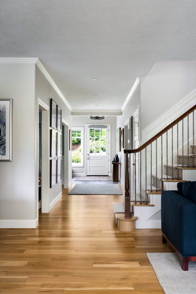 Modern home interior with wooden floors, staircase, and natural light entering through glass front door.