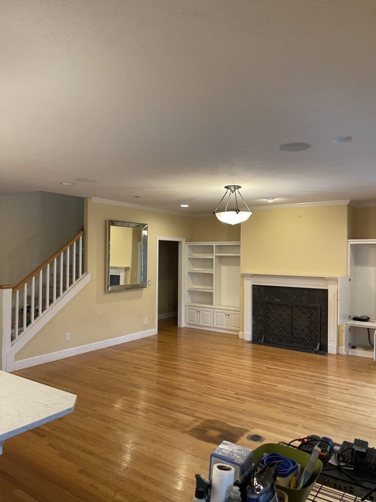 Open living room with hardwood floors, staircase, built-in shelves, mirror, and a fireplace under ceiling light.