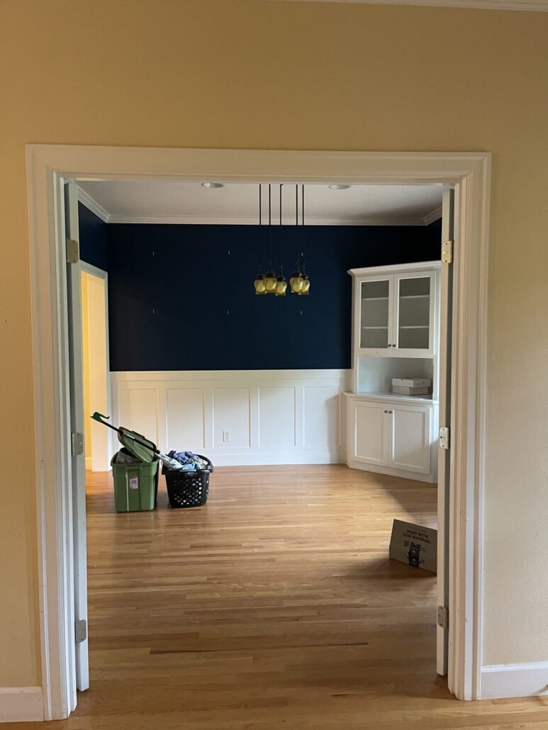 Empty room with wooden floors, dark blue walls, pendant lights, and moving boxes, ready for new decor.