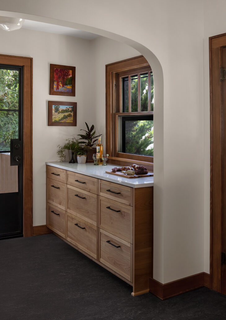 Wooden kitchen corner with countertop, plants, artwork, and window view; natural and cozy design.