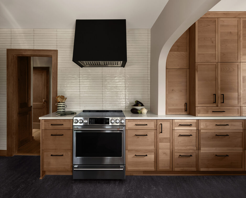 Modern kitchen with stainless steel stove, wooden cabinets, and sleek black range hood.