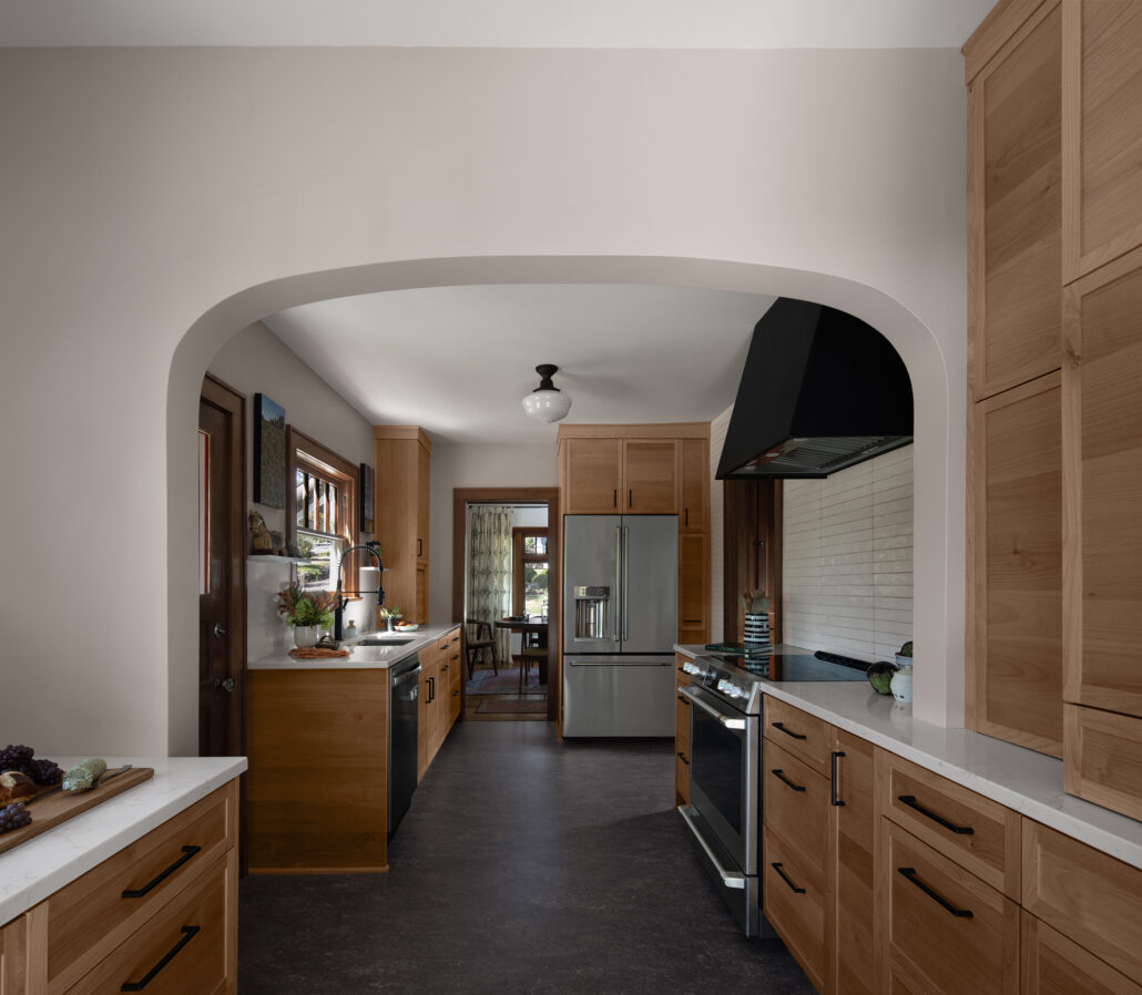 Modern kitchen with wooden cabinets, stainless steel appliances, and an archway leading to the dining area.