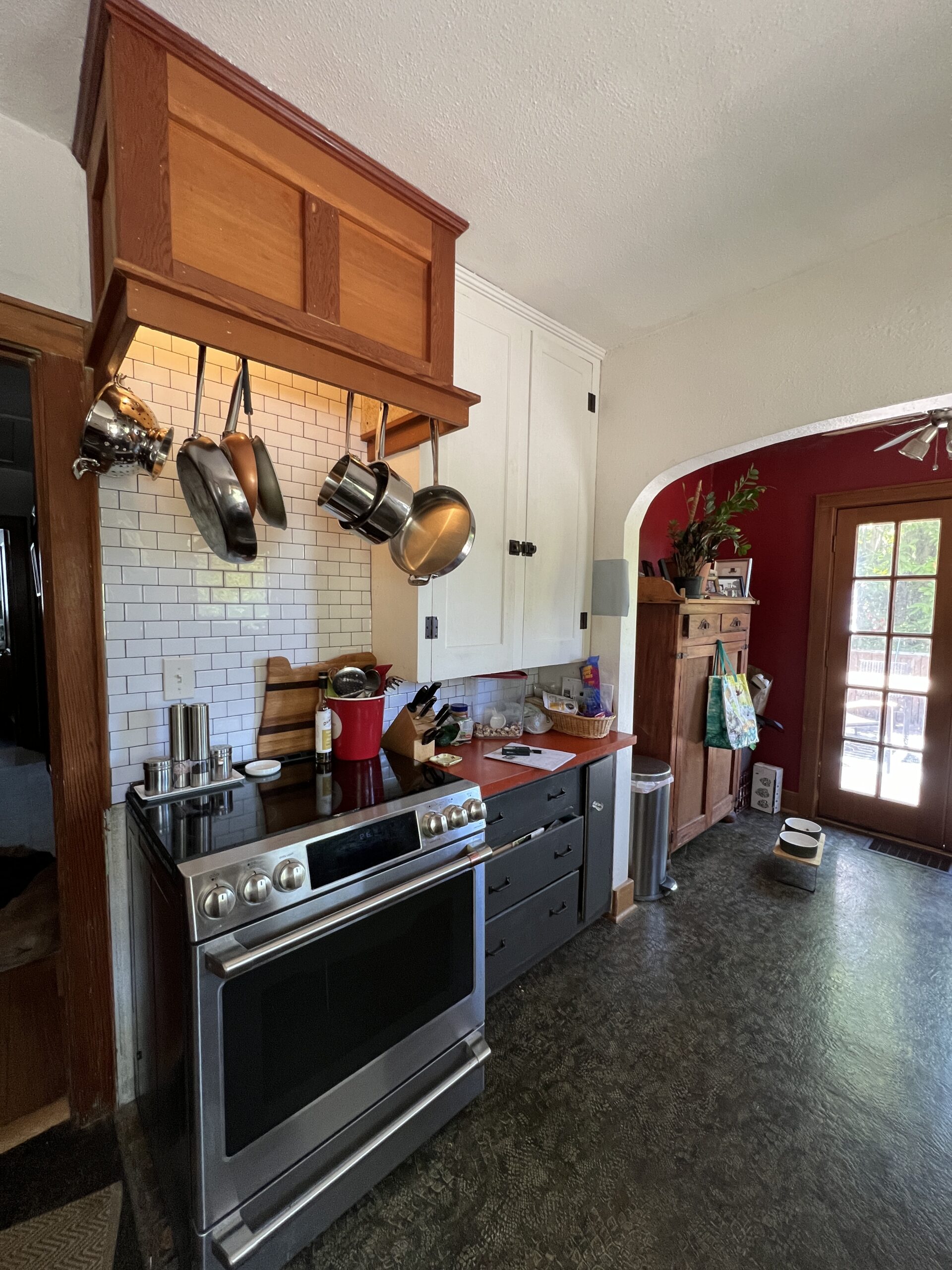 Modern kitchen with stainless steel stove, white subway tiles, and hanging pots. Bright, organized cooking area.