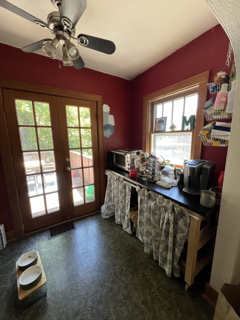 Cozy kitchen nook with red walls, appliances, and a window view. French doors open to greenery outside.